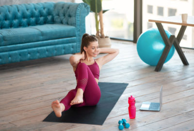Home sports. Strong millennial woman doing abs exercises in front of laptop computer indoors